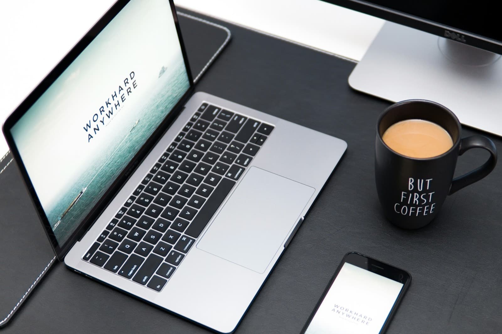 A laptop and a phone side by side on a dark desk, with a coffee mug